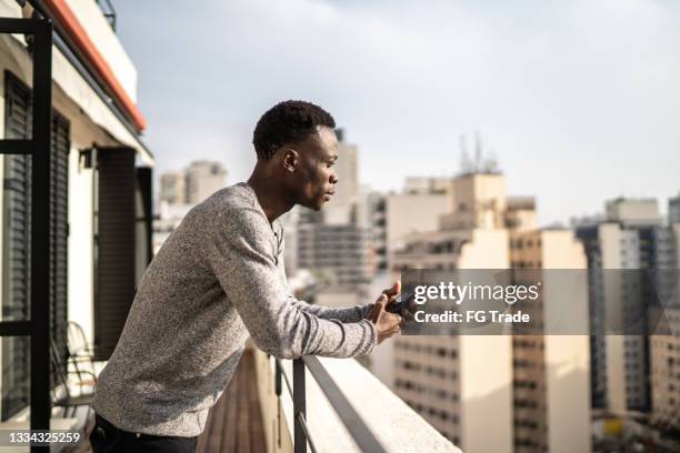 young man contemplating from building terrace - bel appartement stockfoto's en -beelden