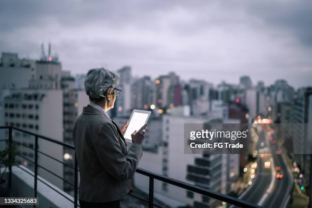 senior businesswoman contemplating and using digital tablet in a rooftop - 63 building stock pictures, royalty-free photos & images