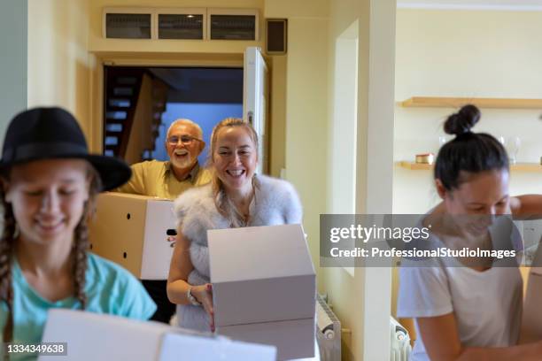 a smiling family is carrying paper boxes into new home on moving day. - new arrival stock pictures, royalty-free photos & images