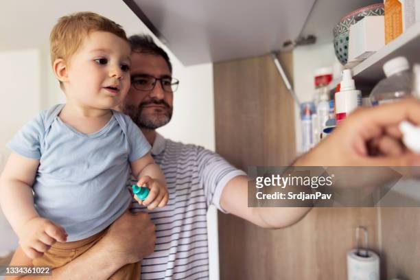 caucasian father and his baby son taking medicines out of the medicine cabinet - bathroom cabinet stock pictures, royalty-free photos & images