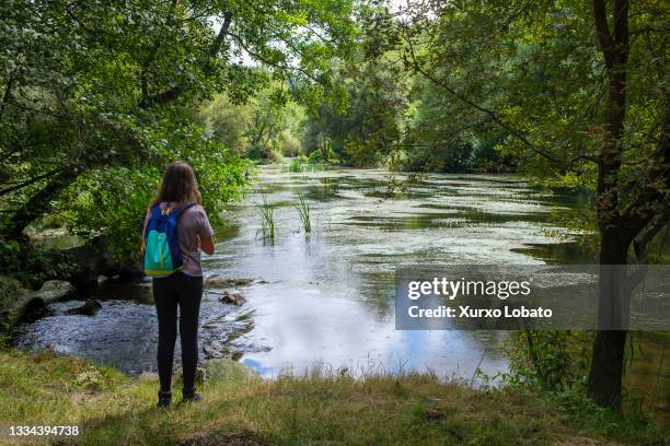 Girl contemplates the landscape of the river Miño with lush forests and trees in the region of Terra Cha. On a break from the hiking trail, seen on...