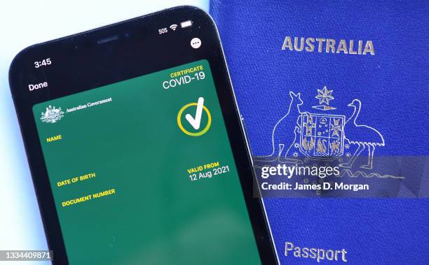 This image has been digitally manipulated.) A mobile phone with an Australian Covid-19 certificate on it next to an Australian passport on August 15,...