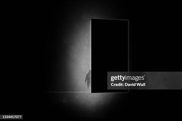 a mystical concept. of a mysterious man silhouetted against light coming through a door. with a minimal dark edit - light coming through doors stock-fotos und bilder