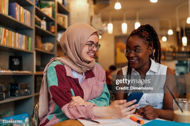 two students having a study session at a cafe table - hijab stock pictures, royalty-free photos & images