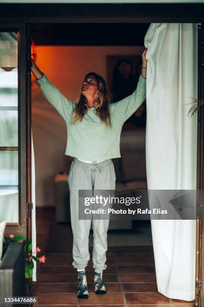 woman opening or closing curtains at home - tracksuit stock pictures, royalty-free photos & images