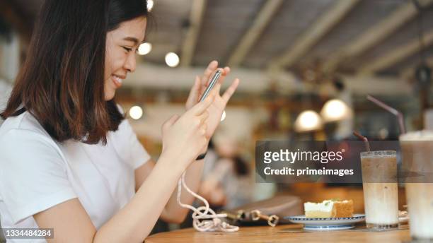 schöne junge asiatische frau genießen es, fotos im café zu machen und auf ihren freund zu warten und kaffee zu trinken und foto in soziales netzwerk hochzuladen lächeln und fröhliches gesicht echte menschen - elegant woman smile stock-fotos und bilder