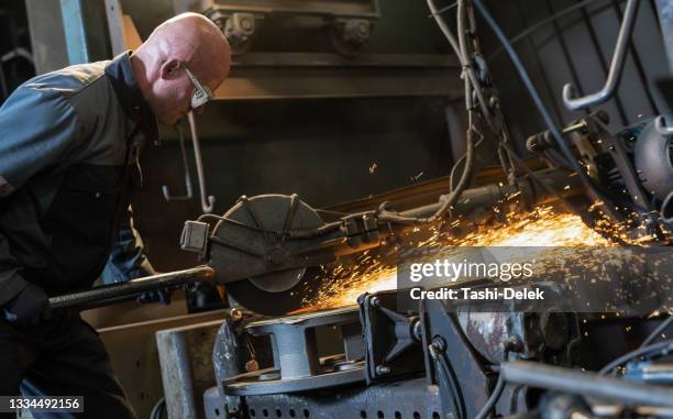 man working with electric hand grinder. producing flow of orange hot glow sparks. dirty and dusty workshop - blacksmith shop stock pictures, royalty-free photos & images