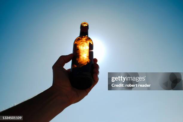 hand holding beer bottle in front of the sun - sunlight through drink glass stock-fotos und bilder