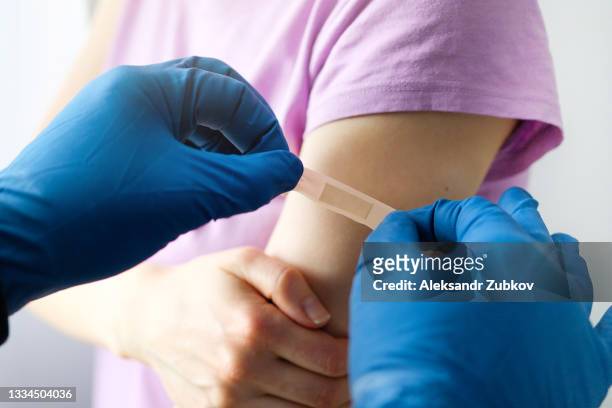 a gloved doctor or health care professional applies a patch or adhesive bandage to a girl or young woman after vaccination or drug injection. the concept of medicine and health care, vaccination and treatment of diseases. first aid services. - 絆創膏 ストックフォトと画像