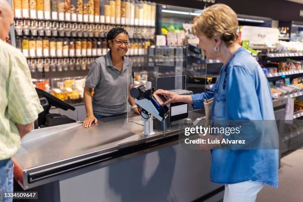 senior female customer buying groceries at a supermarket - ladenkasse stock-fotos und bilder