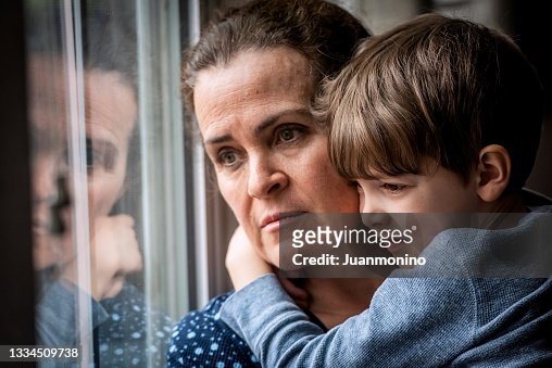 Pensive Mature woman posing with her son, very concerned looking through window worried about loss of her job and eviction due Covid-19 pandemic
