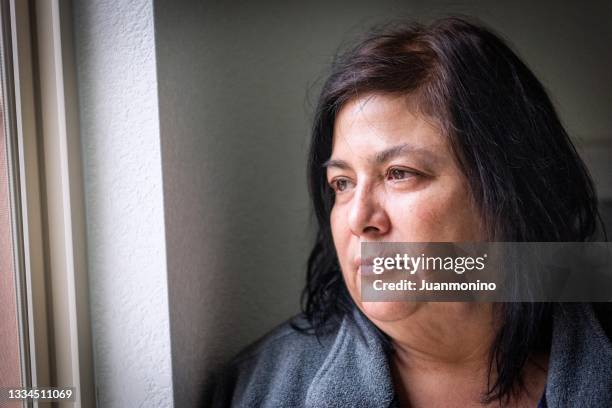 pensive mature woman, very concerned looking through window worried about loss of her job and eviction due covid-19 pandemic - anxiety disorder stock pictures, royalty-free photos & images