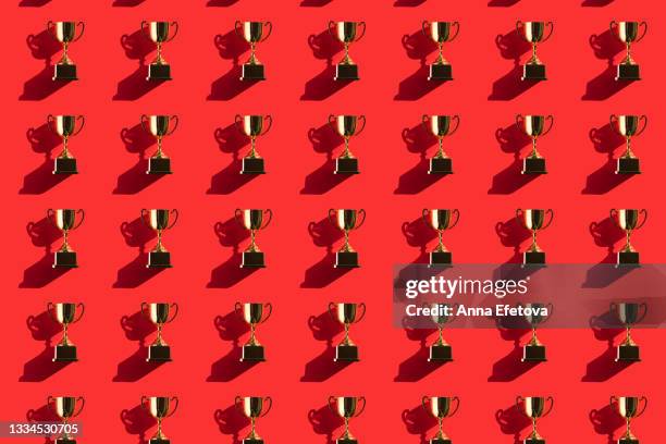 pattern made of metallic golden goblets on red background with shadows. flat lay style - auszeichnung stock-fotos und bilder