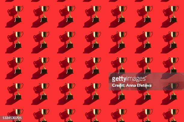 pattern made of metallic golden goblets on red background with shadows. flat lay style - podio del vincitore foto e immagini stock