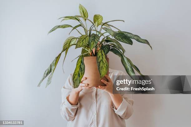 une femme anonyme tenant une grande plante devant son visage - rougir photos et images de collection