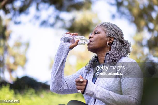 mujer negra mayor bebiendo agua durante el entrenamiento - agua dulce fotografías e imágenes de stock