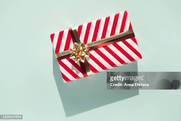 gift box with white-red striped pattern and gold bow on light blue background with shadow. flat lay style and close-up - christmas present stock-fotos und bilder
