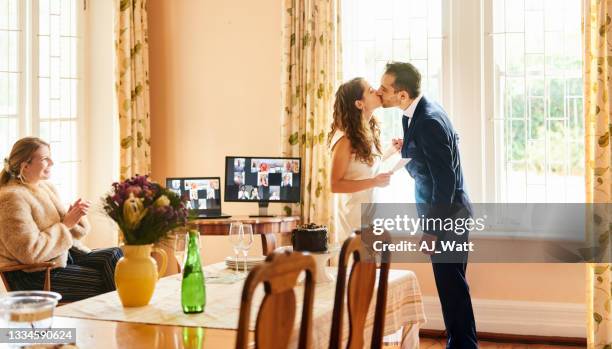 newlyweds kissing while live streaming their wedding online from home - computer wedding stock pictures, royalty-free photos & images