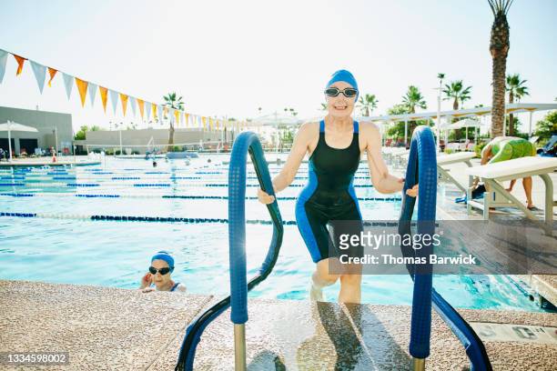 Wide shot of smiling senior female athlete climbing out of swimming pool after early morning workout