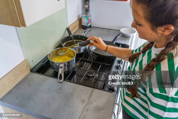 dreizehnjähriges mädchen kocht nudeln im topf - gas cooking stock-fotos und bilder