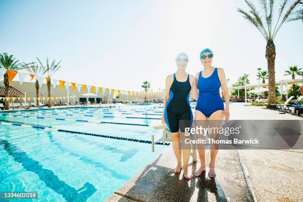 Wide shot portrait of smiling senior friends embracing on pool deck before early morning swim workout