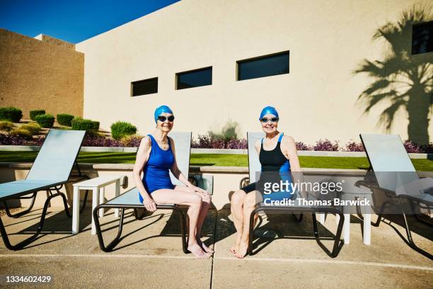 Wide shot portrait of smiling senior friends sitting on pool deck before early morning swim workout