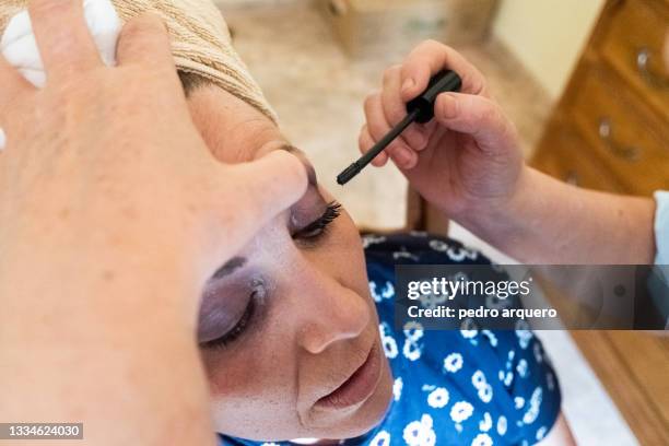 older woman painting her eyelashes with the help of a friend - brow lamination stock pictures, royalty-free photos & images