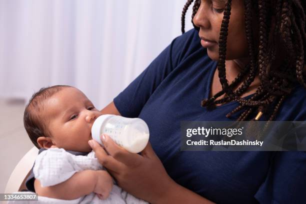 愛らしい女の赤ちゃんのショットは、彼女の母親によって自宅で牛乳をボトル供給されています。 - baby bottle ストックフォトと画像