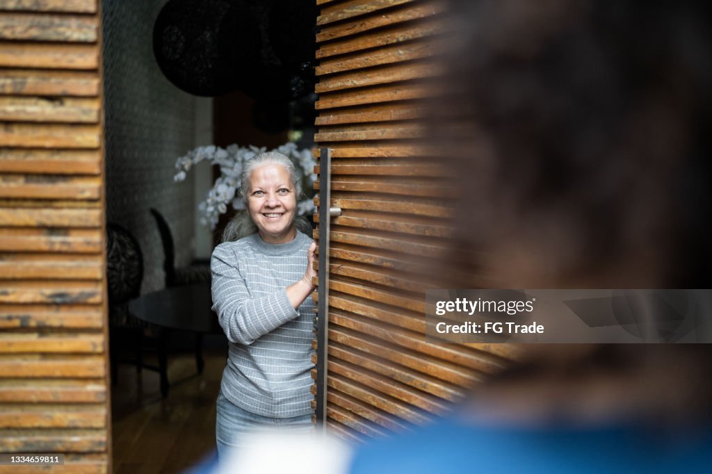 Senior woman open door to healthcare worker arriving at home