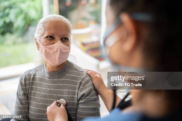 nurse listening to senior patient's heartbeat during home visit - wearing protective face mask - listening to heartbeat 個照片及圖片檔