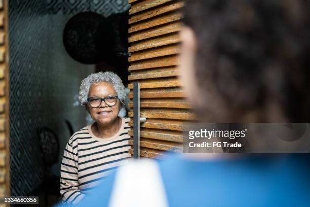 une femme âgée ouvre la porte à l’arrivée d’un travailleur de la santé à la maison - entrance hall photos et images de collection