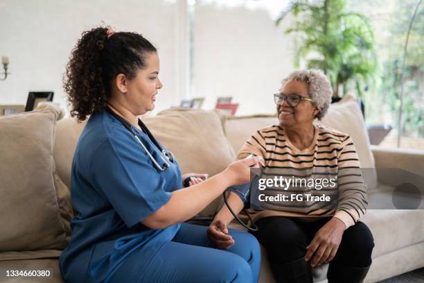 healthcare worker taking blood pressure of senior woman at home - hypertensive stockfoto's en -beelden
