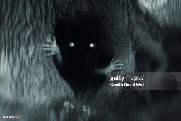 a spooky horror concept of a monster with glowing eyes, hiding in a tree trunk, in a dark spooky forest. with a grunge, blurred, edit. - spooky stock-fotos und bilder