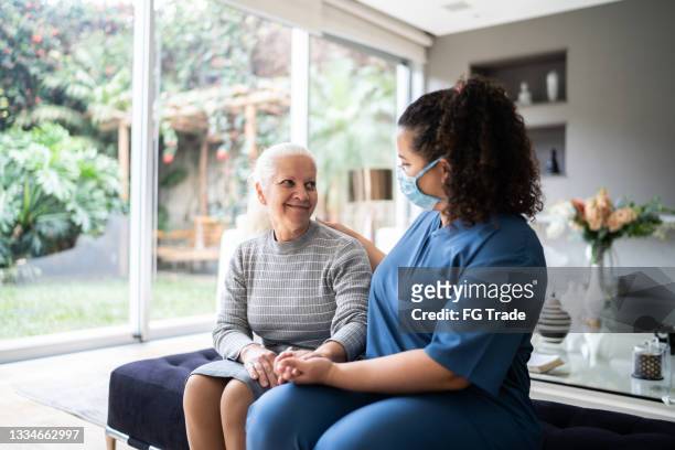 trabajador de la salud hablando y consolando a un paciente mayor durante una visita domiciliaria - nurse with mask fotografías e imágenes de stock