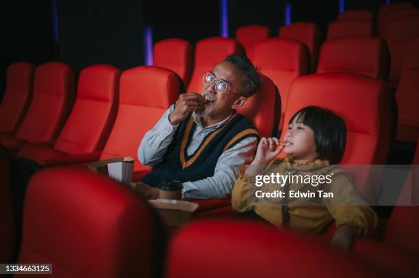 asian chinese active senior man and his granddaughter enjoy watching movie in cinema movie theatre - asian watching movie stock pictures, royalty-free photos & images