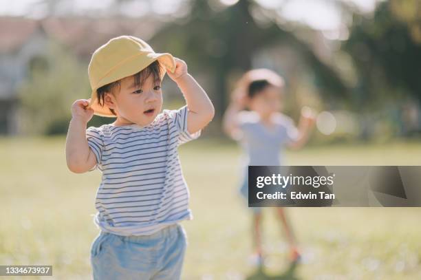 cute asian chinese baby boy wearing yellow hat at public park in the morning - asian twins stockfoto's en -beelden