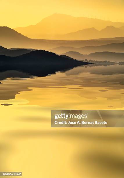 sunset with the sun hidden among the silhouettes of mountains next to a lake. - dramatic landscape stock pictures, royalty-free photos & images