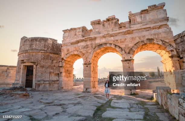 photographer tourist is smiling  in front of the frontinus gate in ancient ruins in hierapolis , pamukkale - oude ruïne stockfoto's en -beelden