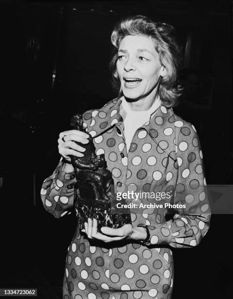 American actress Lauren Bacall , wearing a polka dot outfit, holding the 'Best Musical' statuette for 'Applause', at the Evening Standard Theatre...