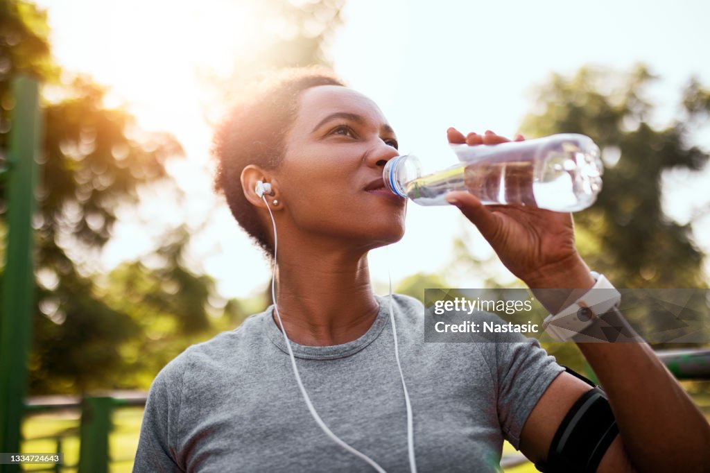 African American woman jogger drinking water hydrating in morning time
