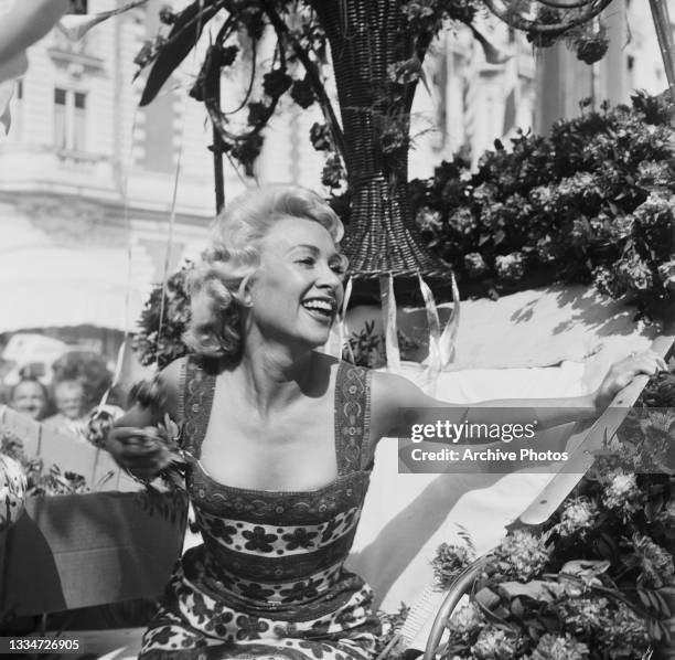 French actress Martine Carol smiling from a carriage during La Bataille des Fleurs flower parade at the 9th Cannes Film Festival in Cannes, France,...
