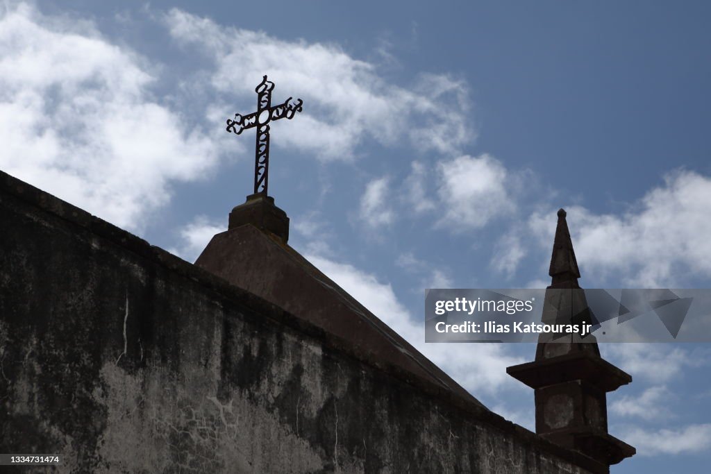 Church spire and cross against blue cloudy sky, behind wall