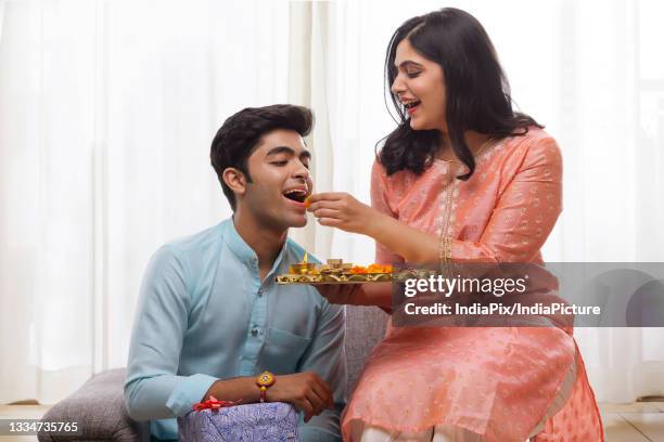 a happy young woman giving sweets to brother on rakshabandhan - akhi stock pictures, royalty-free photos & images