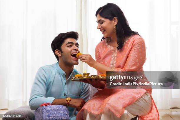 a happy sister giving sweets to brother on rakshabandhan - raksha bandhan stock pictures, royalty-free photos & images