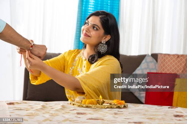 a happy young woman looking above and tying rakhi - rakhi stock pictures, royalty-free photos & images