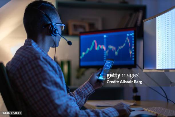 man looking at currency trading app on his smart phone from his home office - geld technisch mensch stock-fotos und bilder