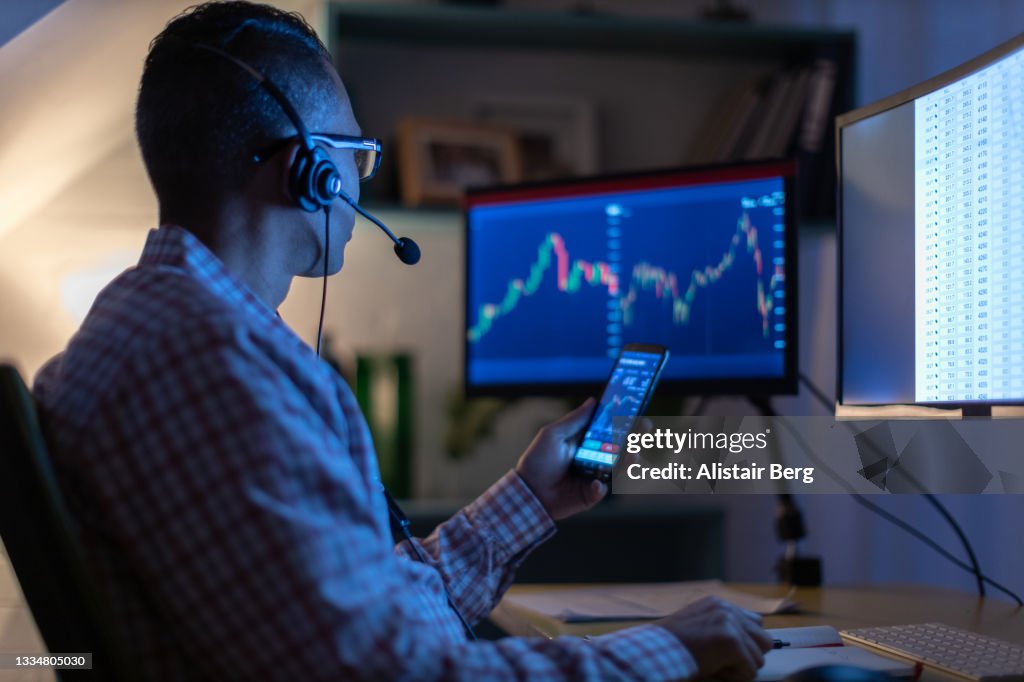 Man looking at currency trading app on his smart phone from his home office
