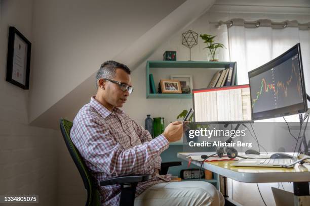 man looking at currency trading app on his smart phone from his home office - smart numbers office stockfoto's en -beelden