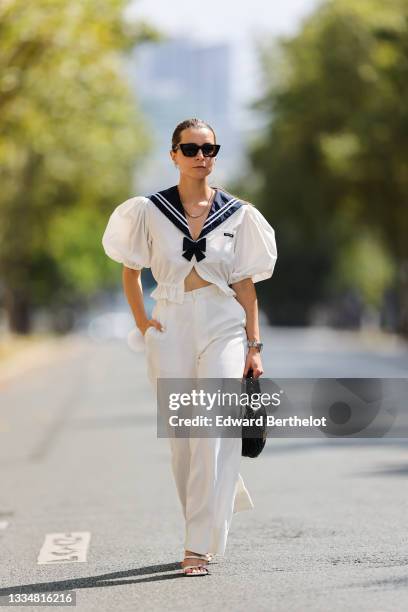 Julia Comil wears a white cropped blouse sailor with bow and puffed sleeves by Miu Miu, high waisted white palazzo pants, white sandals from By Far,...