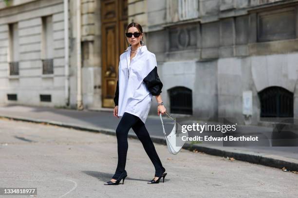 Julia Comil wears an oversized cotton white and black shirt with triangle Prada logo and zipped by Prada, black leggings, a Cleo white patent leather...